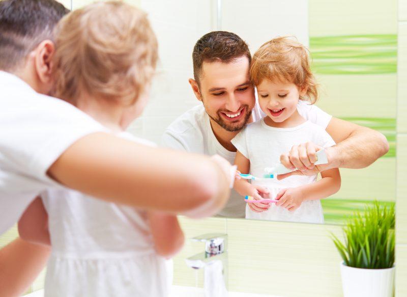 Happy Family Father And Child Girl Brushing Her Teeth In Bathroo